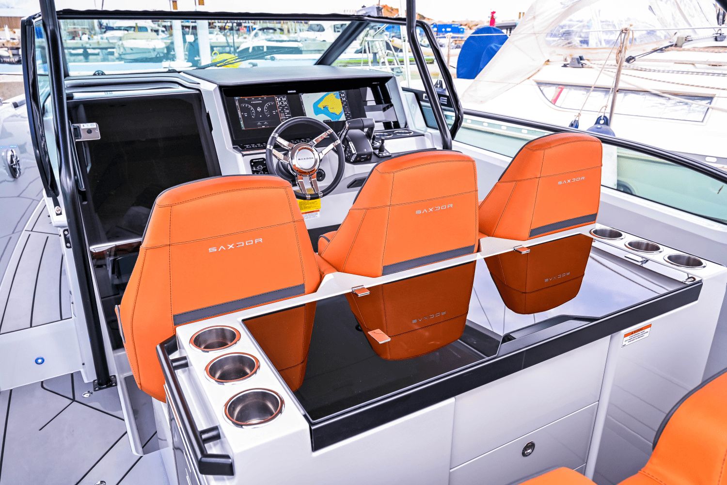 The image shows the cockpit of a Saxdor SX320 GTO with three orange seats and a modern helm.