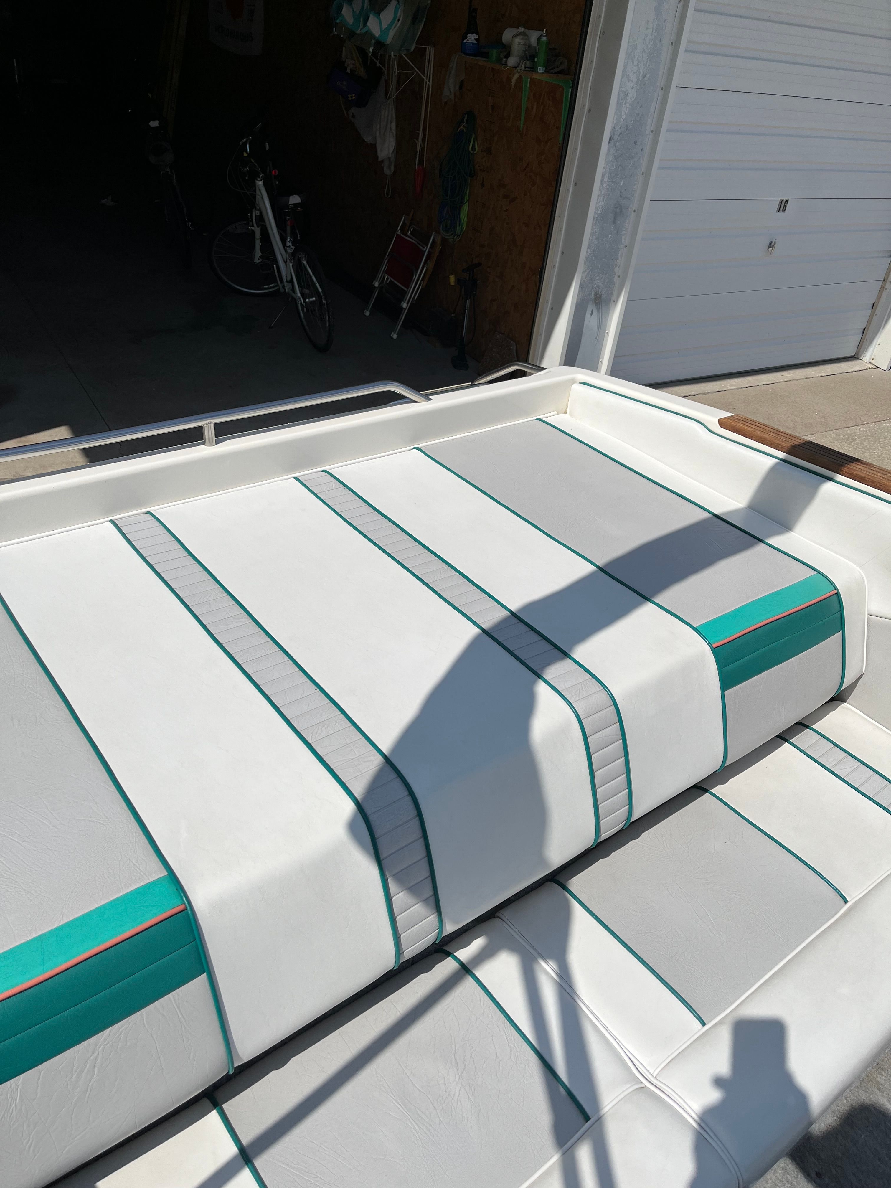 A white boat with turquoise stripes is parked in a garage.