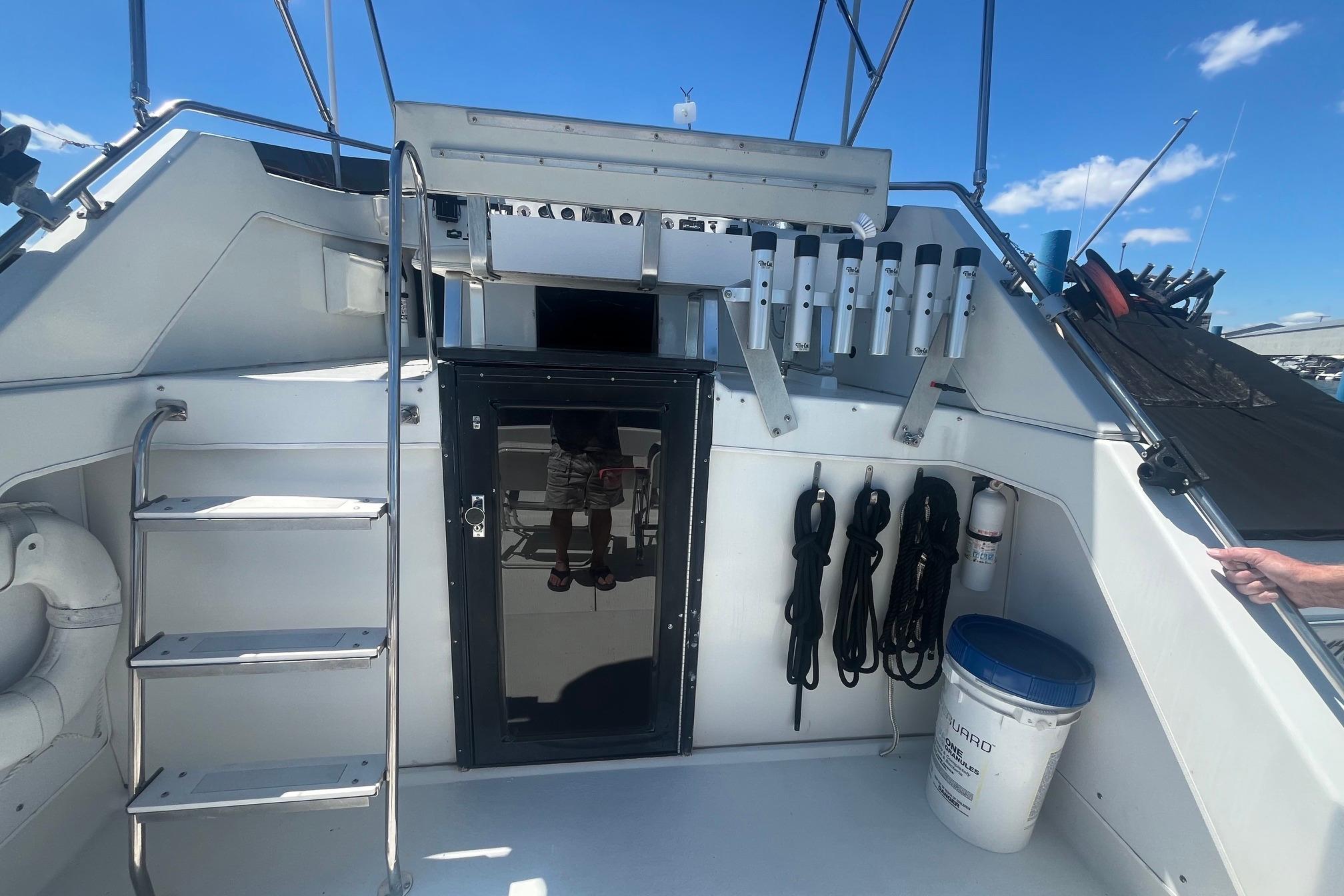 1988 Seafox 29 Flybridge boat deck with storage, ladder, and equipment under a clear blue sky.