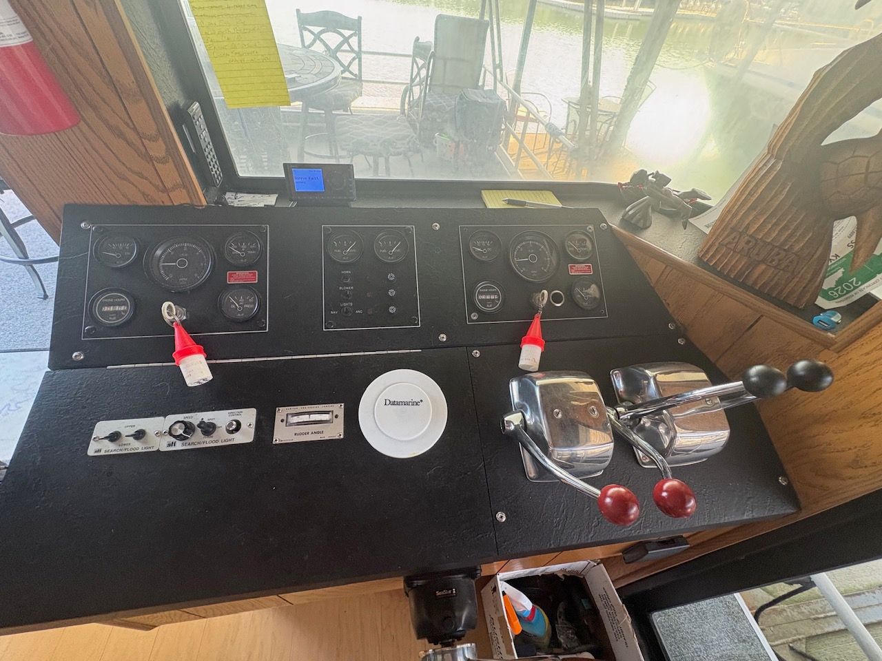 The image shows the helm of a houseboat with various instruments and levers.