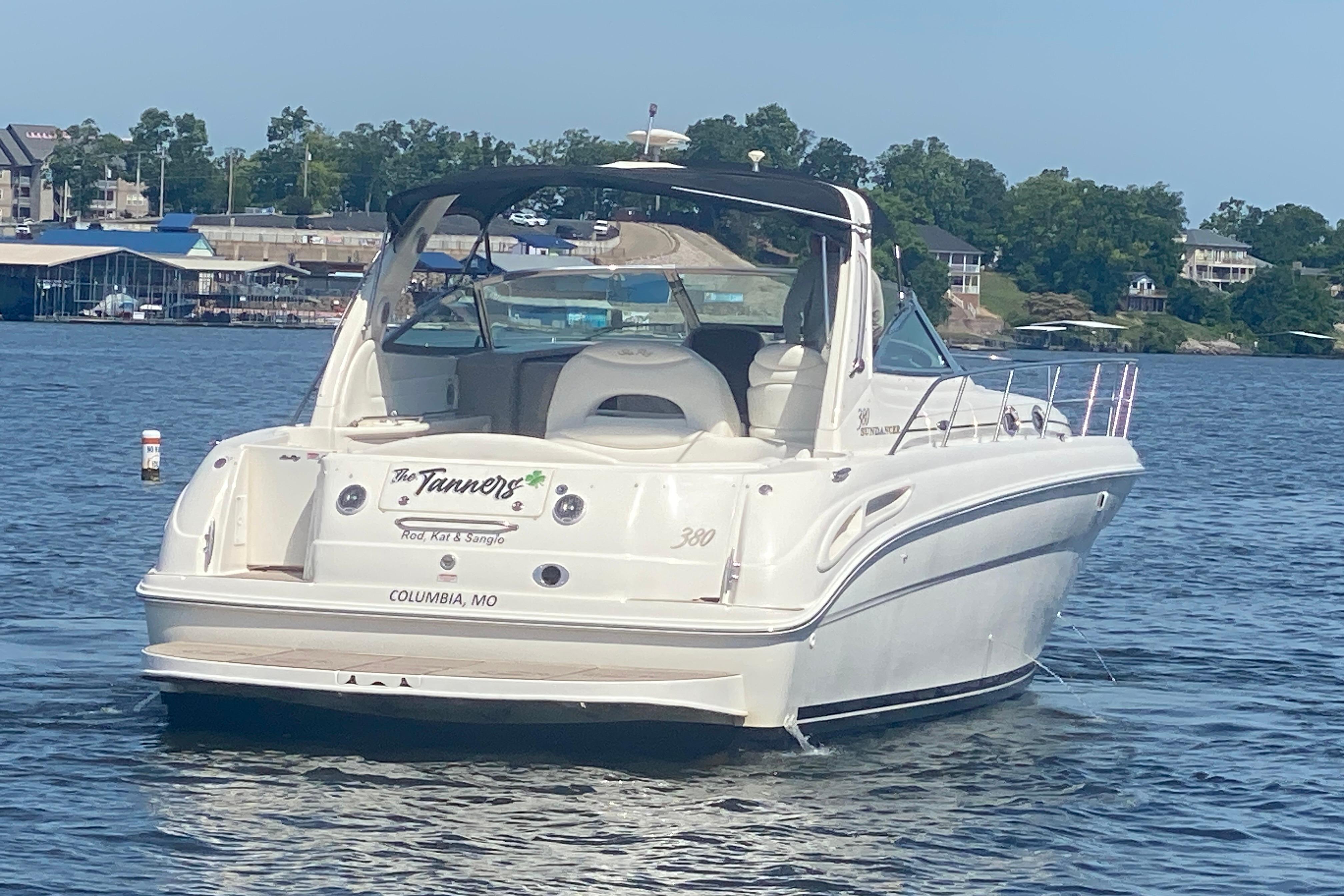 2004 Sea Ray 380 Sundancer boat on a lake, with marina and trees in the background.