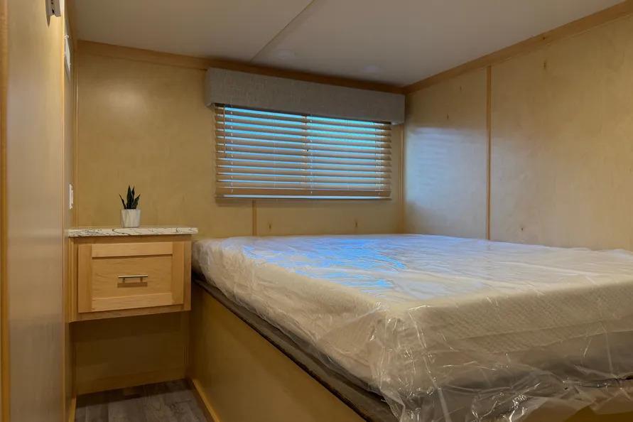 Bedroom interior of 2026 Sumerset Voyager with bed, window blinds, and side table.