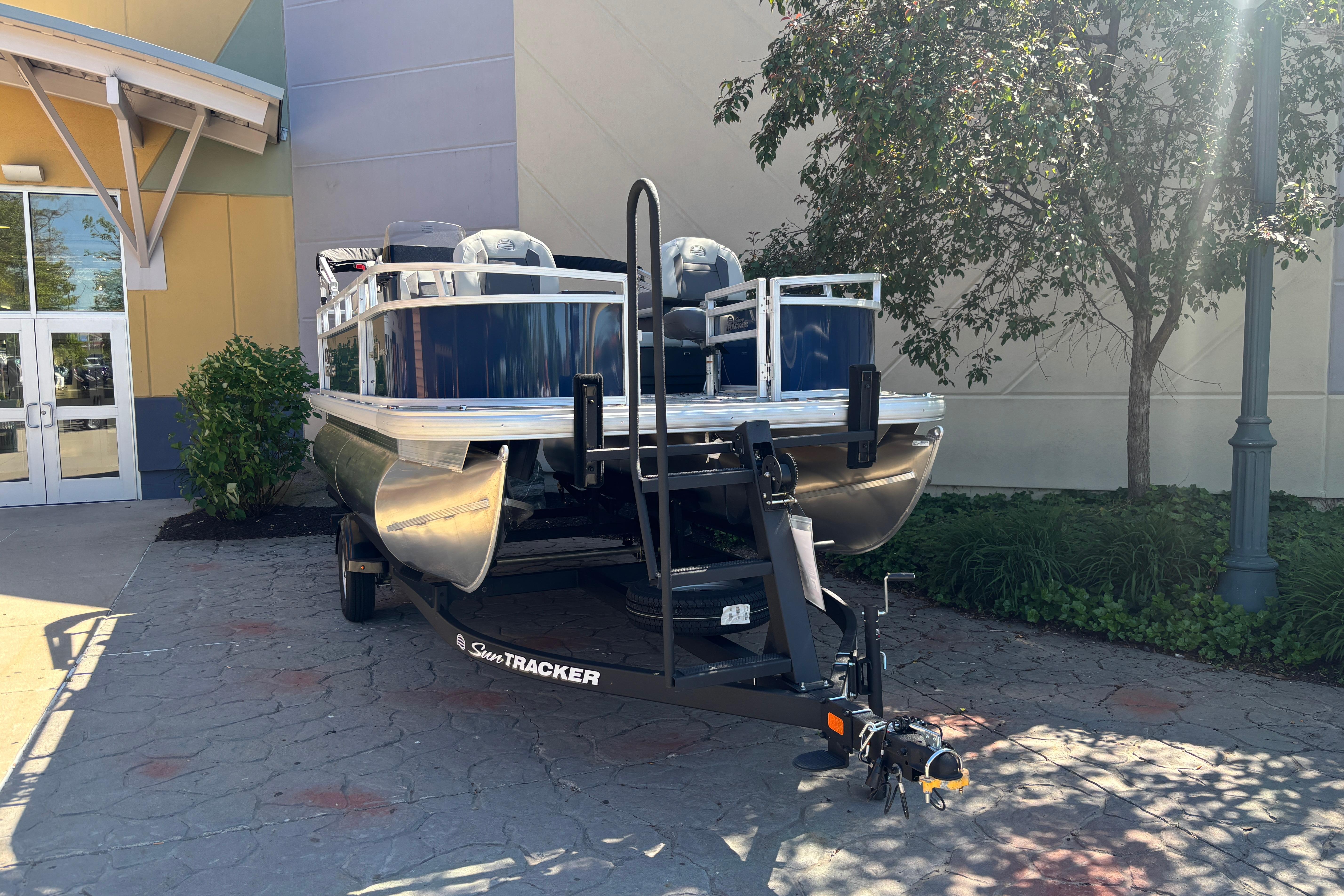 2026 Sun Tracker Bass Buggy 16 XL Select pontoon boat on trailer, parked outdoors.