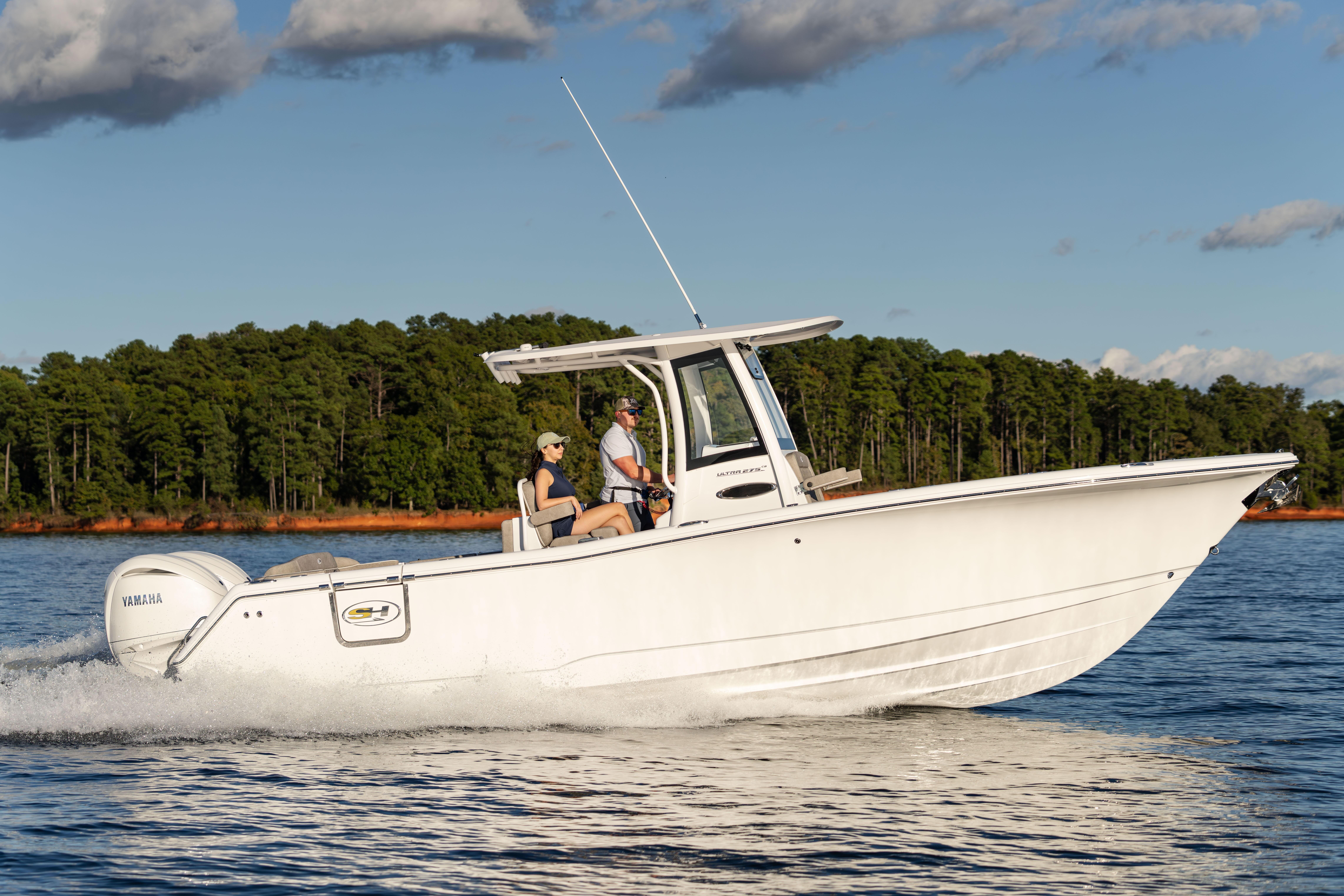 2026 Sea Hunt Ultra 275 Coffin Box boat cruising on a lake with forested shoreline.