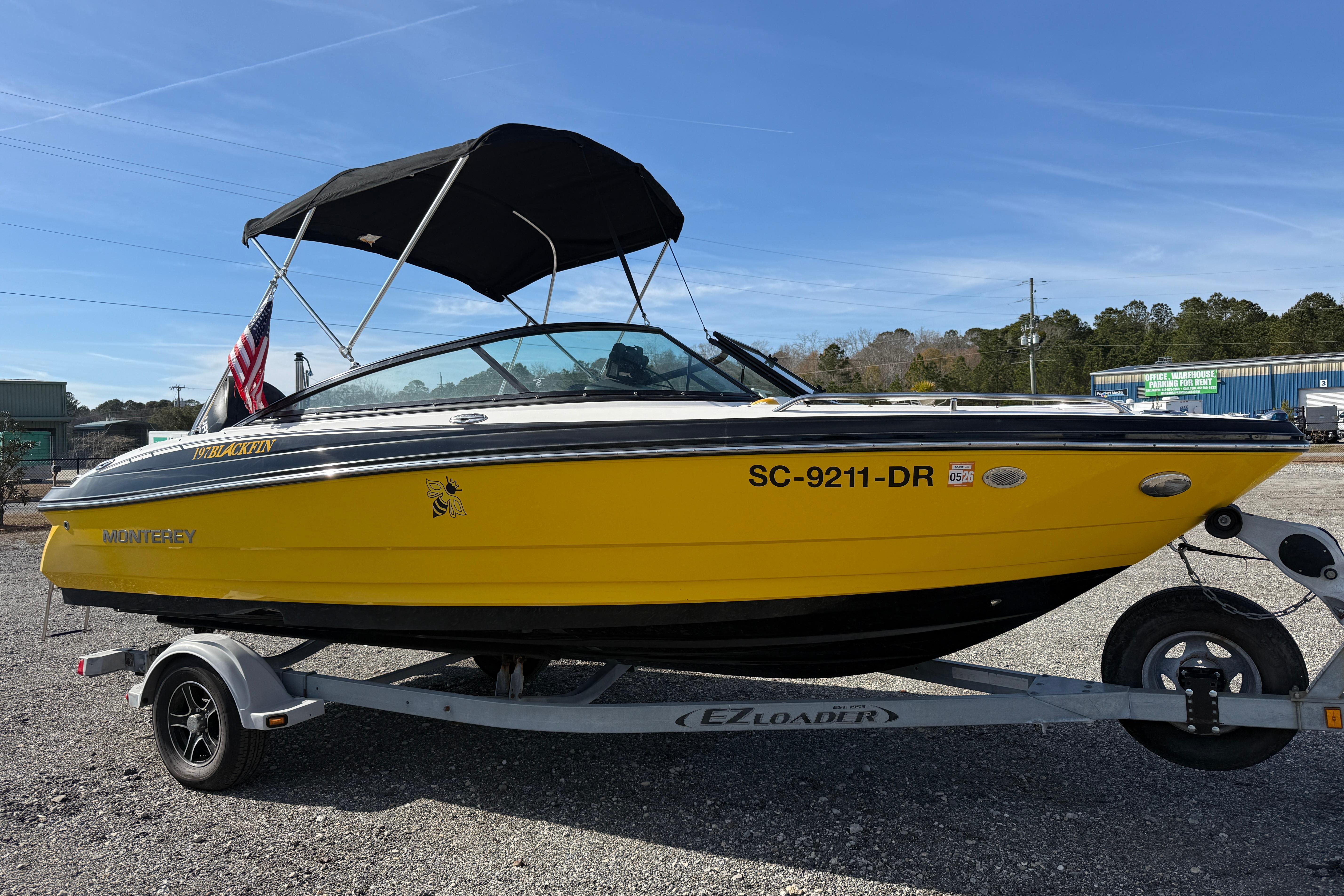Yellow 2014 Monterey 197 Blackfin boat on trailer, with canopy and American flag.