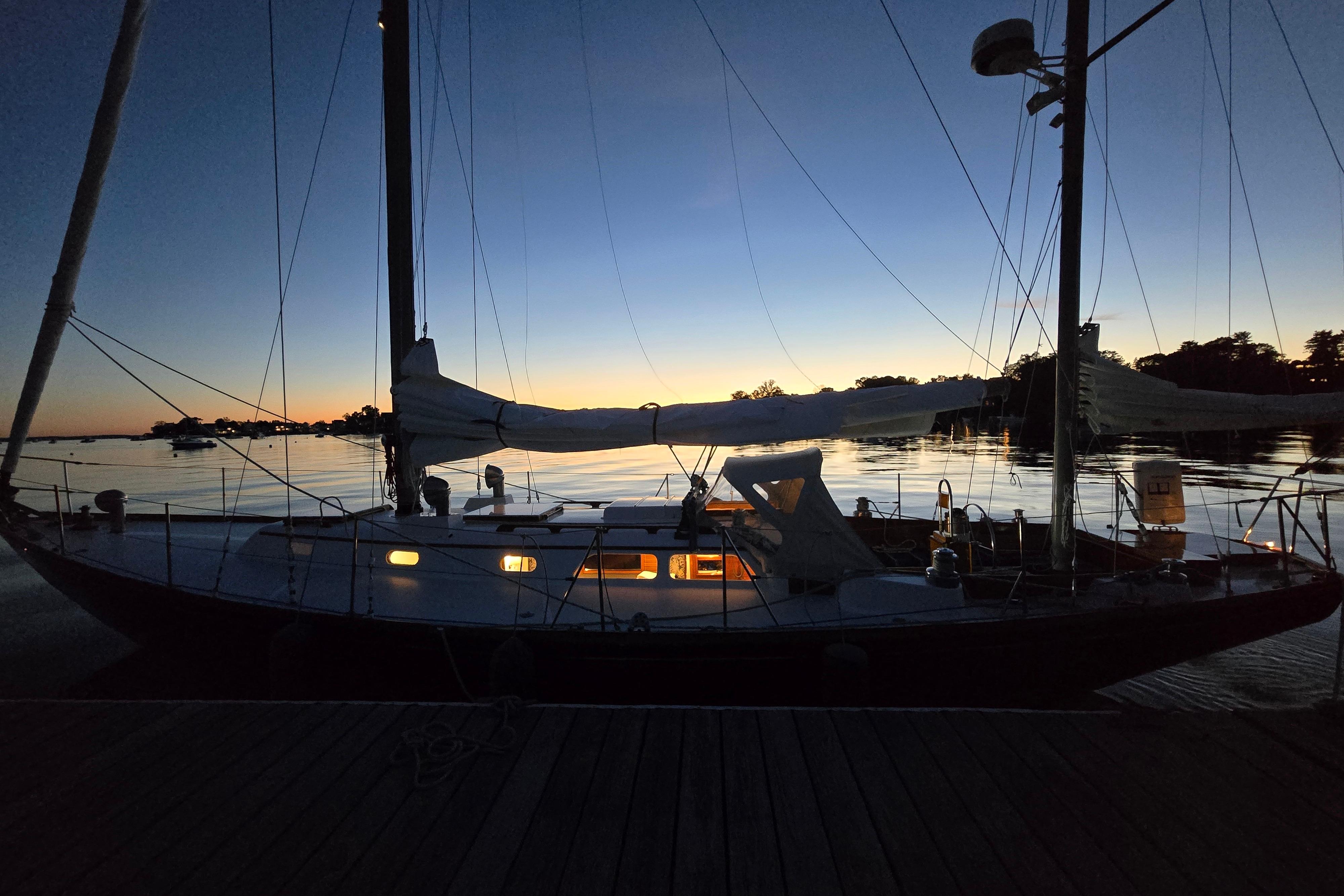 1970 Hinckley Bermuda 40 sailboat docked at sunset, silhouetted against a serene water backdrop.
