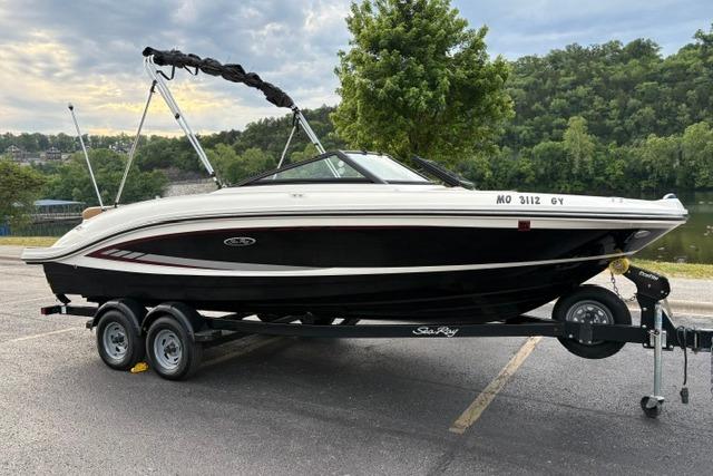 2017 Searay SPX210 boat on trailer, parked near a scenic lake with lush greenery.